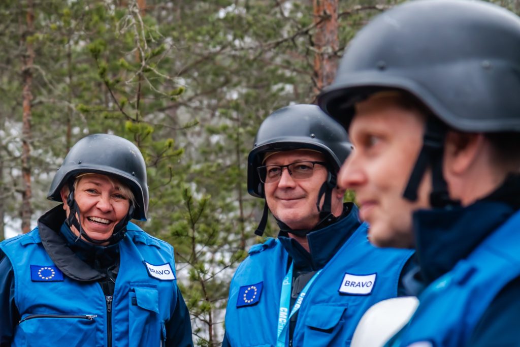 3 individuals wearing training gear, helmets and blue vests