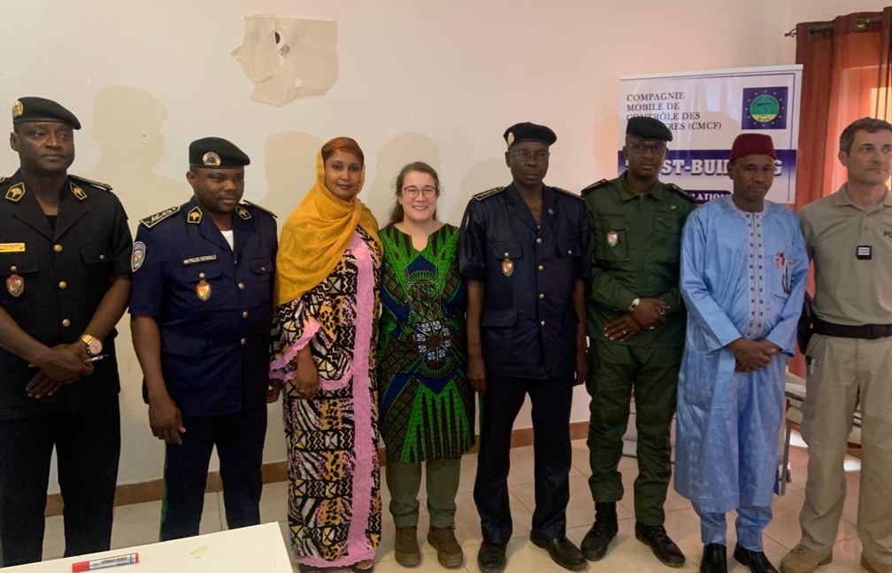 Ryhmäkuvassa miehiä sekä naisia poliisin univormuissa ja perinteisissä nigeriläisissä vaatteissa. Kirjoittaja Meri Paunonen on kuvassa keskellä paikallisten kumppaneidensa ympäröimänä.